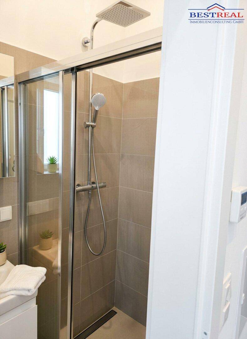 Moderne Duschkabine mit Regendusche und Handbrause, komplett gefliest in hellen Farbtönen.