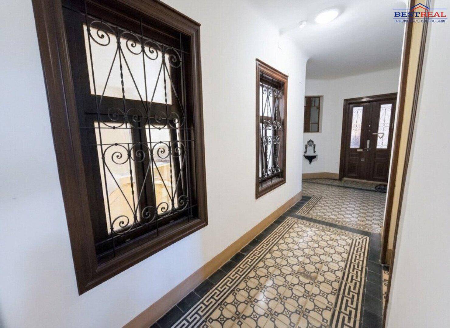 Historischer Eingangsbereich mit kunstvollen Fliesen und verzierten Holzfenstern, sehr elegant und gepflegt.
