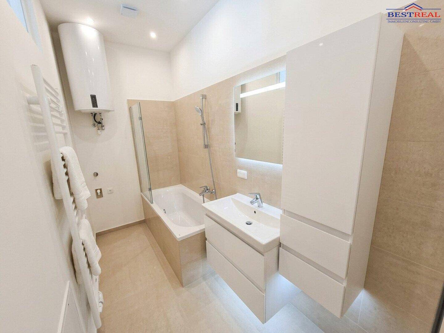 Modernes Badezimmer mit Badewanne, Waschtischunterschrank und Wandheizkörper, hell gefliest.