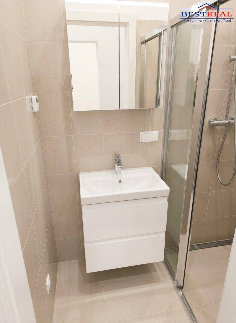 Modernes Badezimmer mit Waschtisch, Spiegelschrank und Duschbereich, hell gefliest und funktional.
