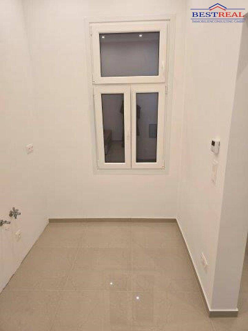 Heller, leerer Raum mit Fenster und Fliesenboden, vorbereitet für Installationen.