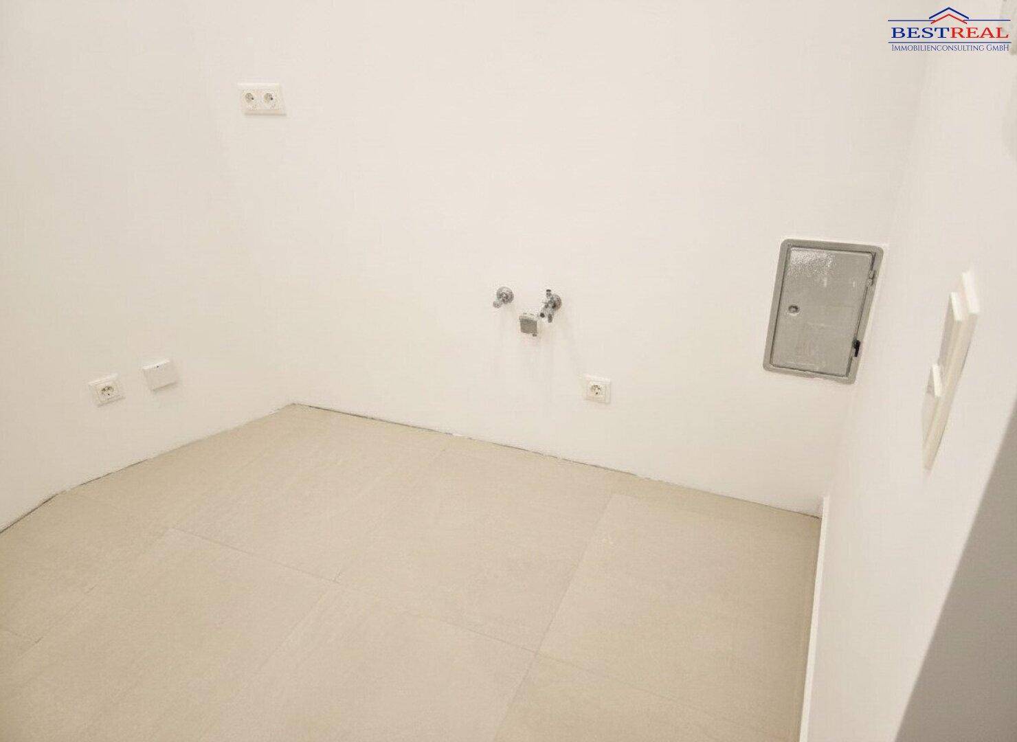 Leerer Raum mit Fliesenboden und Anschlüssen für Haushaltsgeräte, hell und funktional.