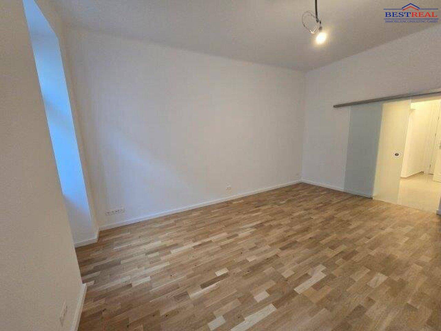 Heller Raum mit Eichenparkett und weiß gestrichenen Wänden, mit Schiebetür.