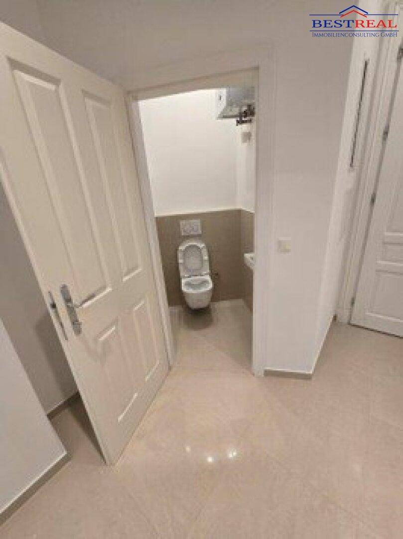 Kleines Gäste-WC mit Wand-WC und Handwaschbecken, hell gefliest und modern gestaltet.