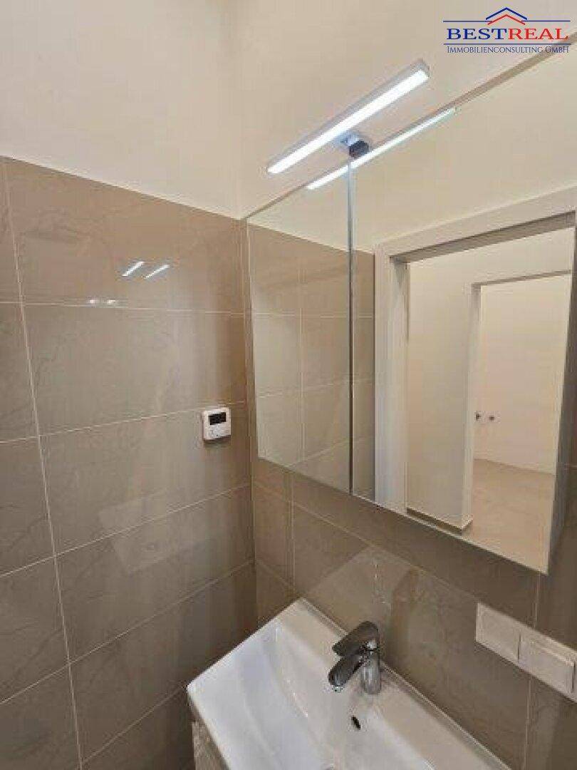 Modernes Badezimmer mit Waschbecken, großem Spiegel und Wandfliesen in Beige.
