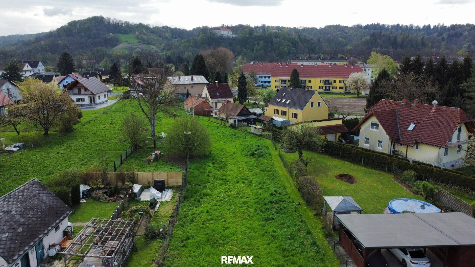 Panoramablick auf ein großes, grünes Baugrundstück umgeben von Einfamilienhäusern und Natur.