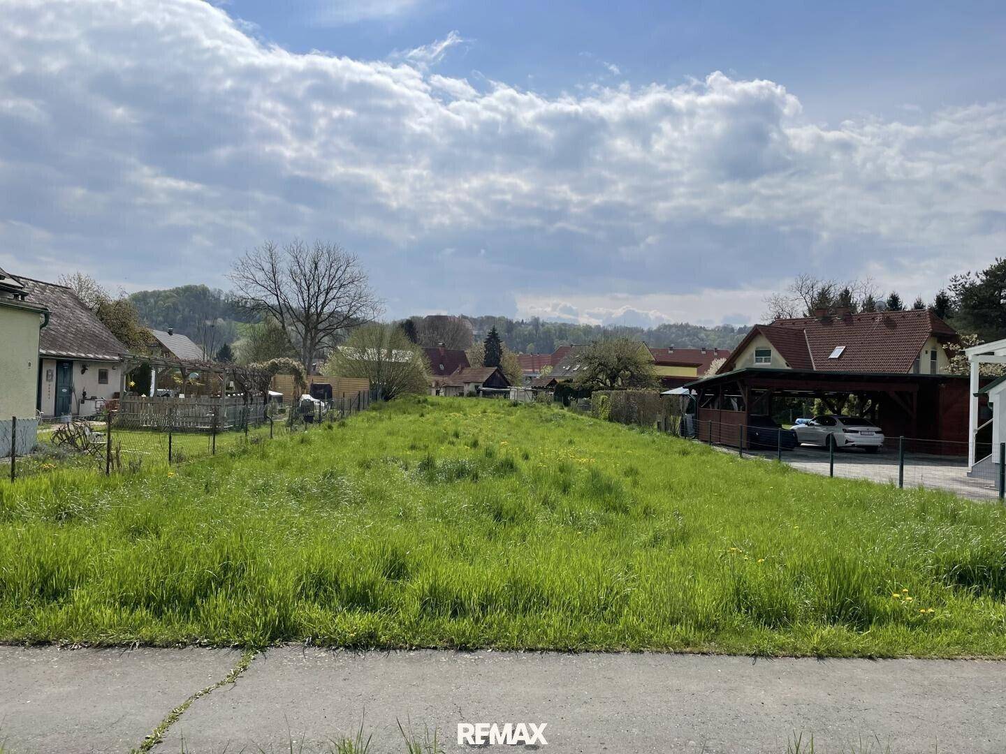 Sonniges, grünes Grundstück mit weitem Blick auf die ländliche Umgebung und angrenzende Wohnhäuser.