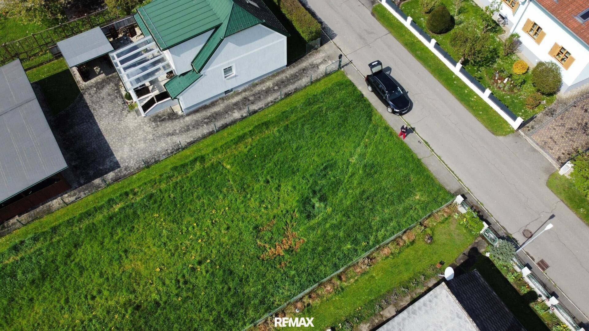 Senkrechte Luftaufnahme des grünen Grundstücks, angrenzend an eine Straße und ein Wohnhaus mit Garten.