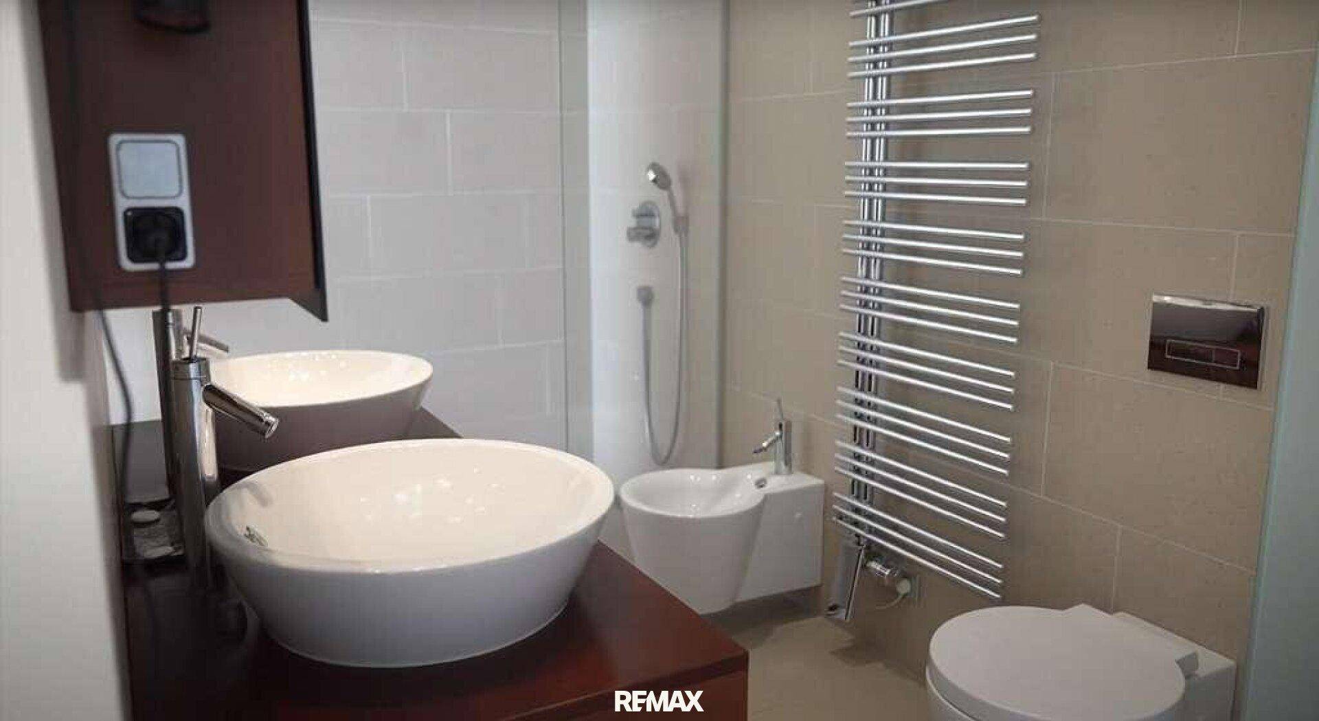 Modernes Badezimmer mit zwei Aufsatzwaschbecken, Bidet, Dusche und Handtuchheizkörper.