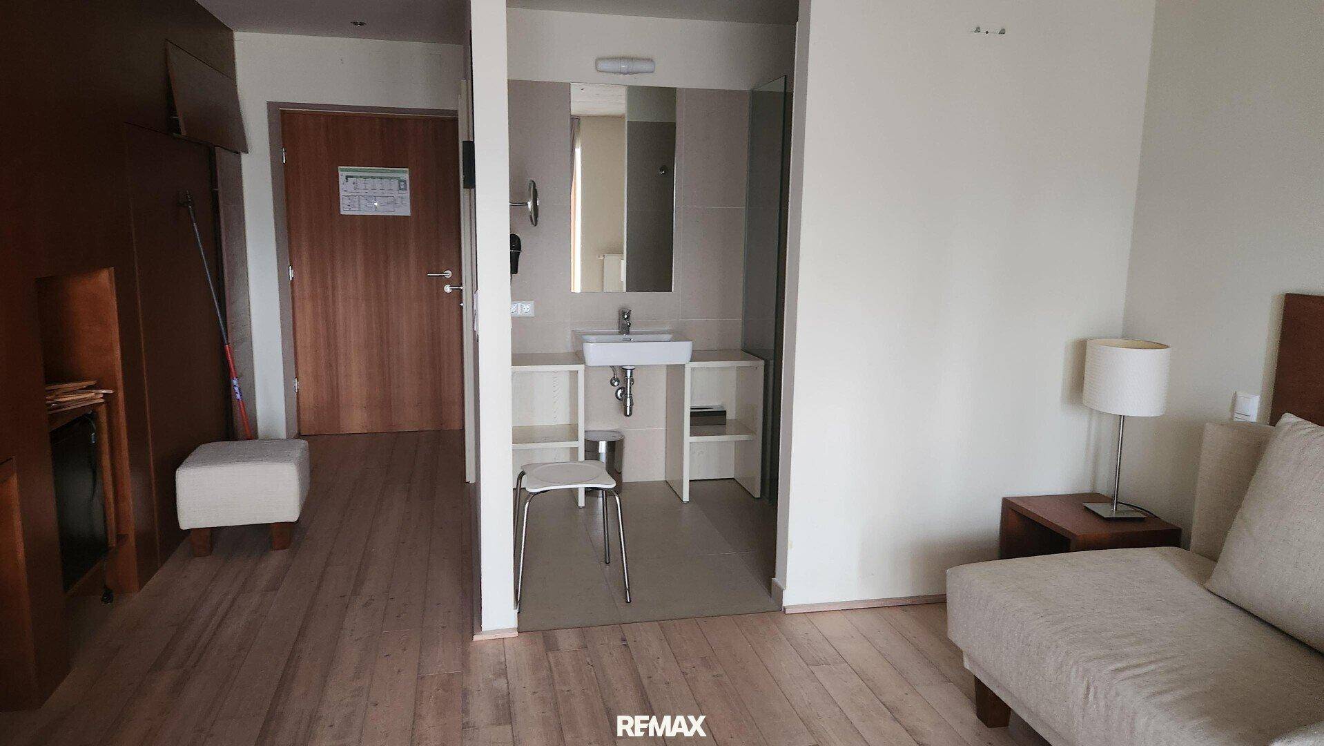 Schlafzimmer mit Sofa und offenem Zugang zu einem Badezimmerbereich mit Waschtisch.