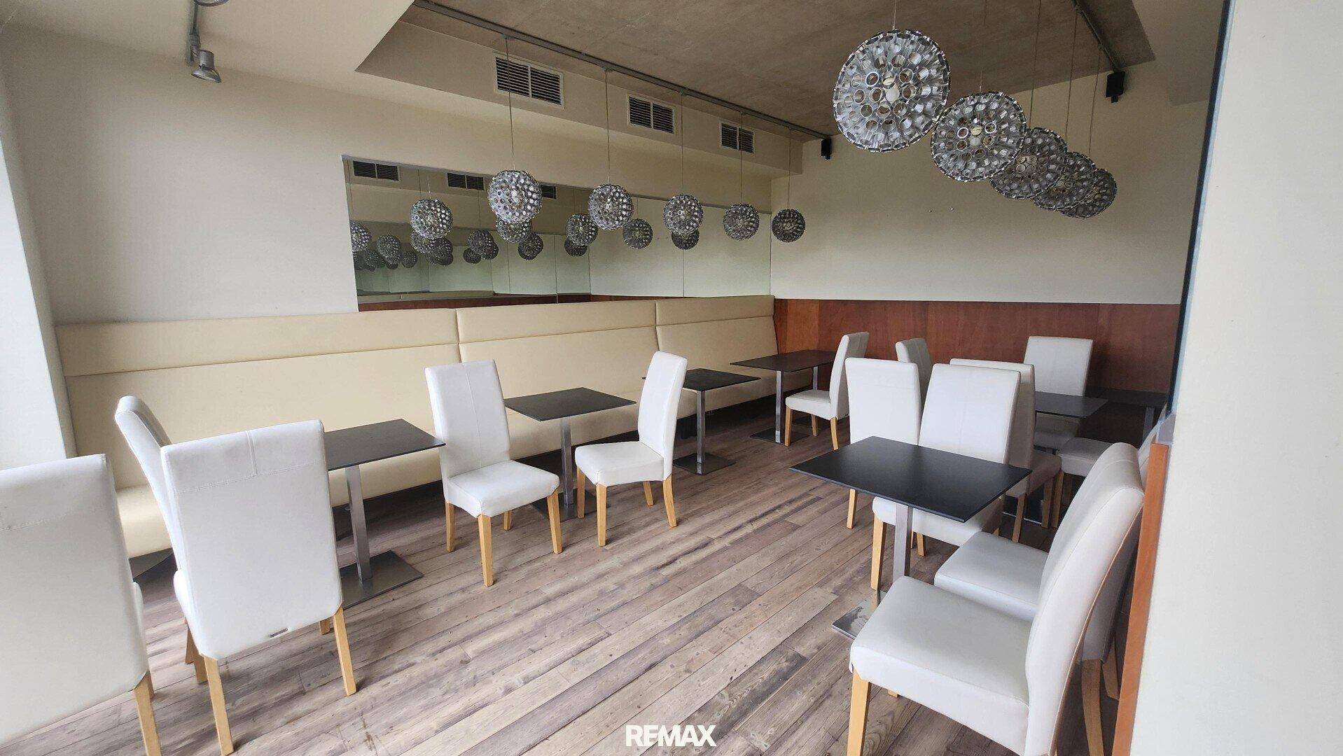 Gemütlicher Restaurantbereich mit Sitzbänken, kleinen Tischen und dekorativen Hängelampen.