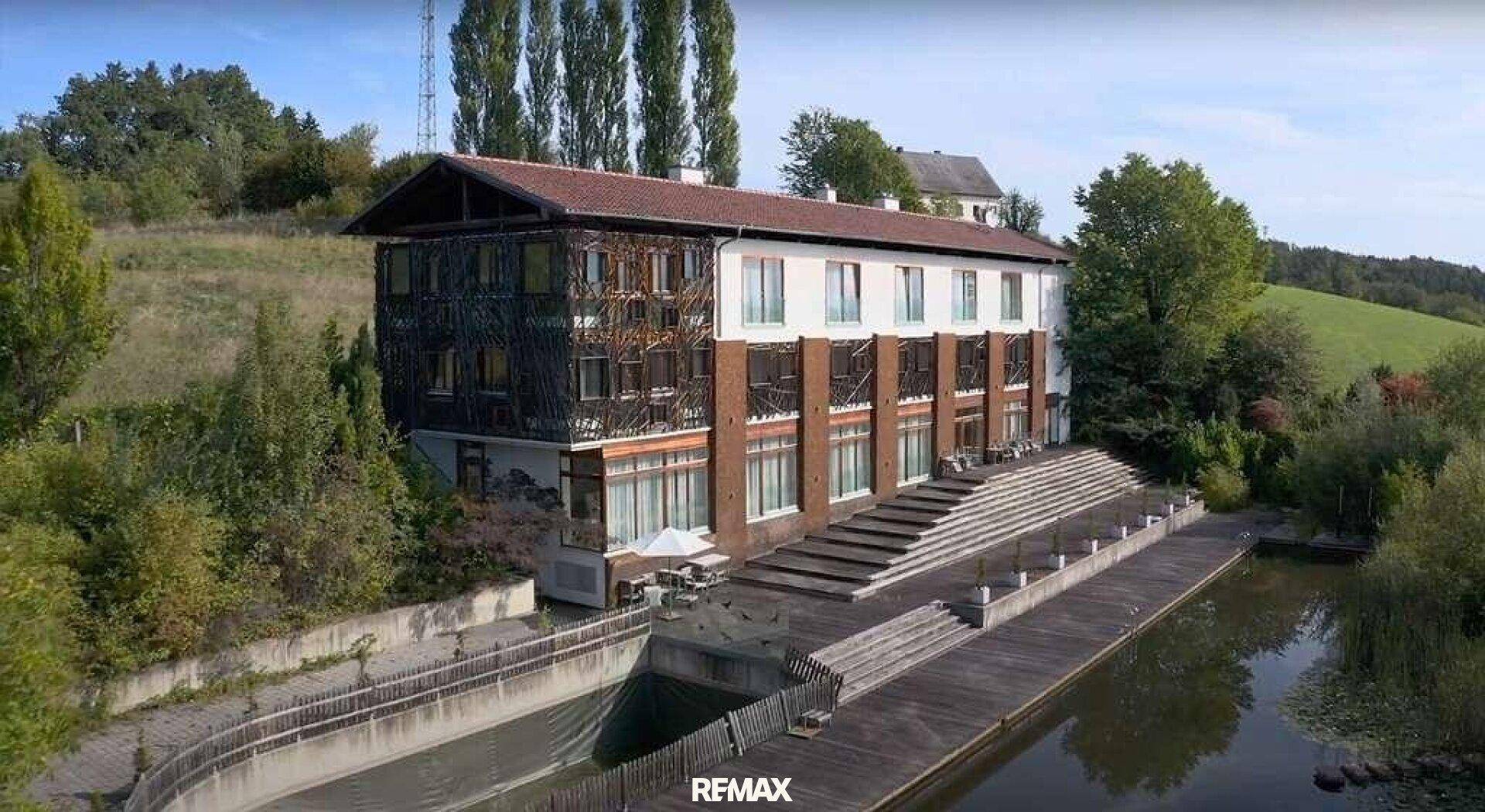 Ansicht des Gebäudes mit Holzfassade, großen Fenstern und einer Holzterrasse am Wasser.