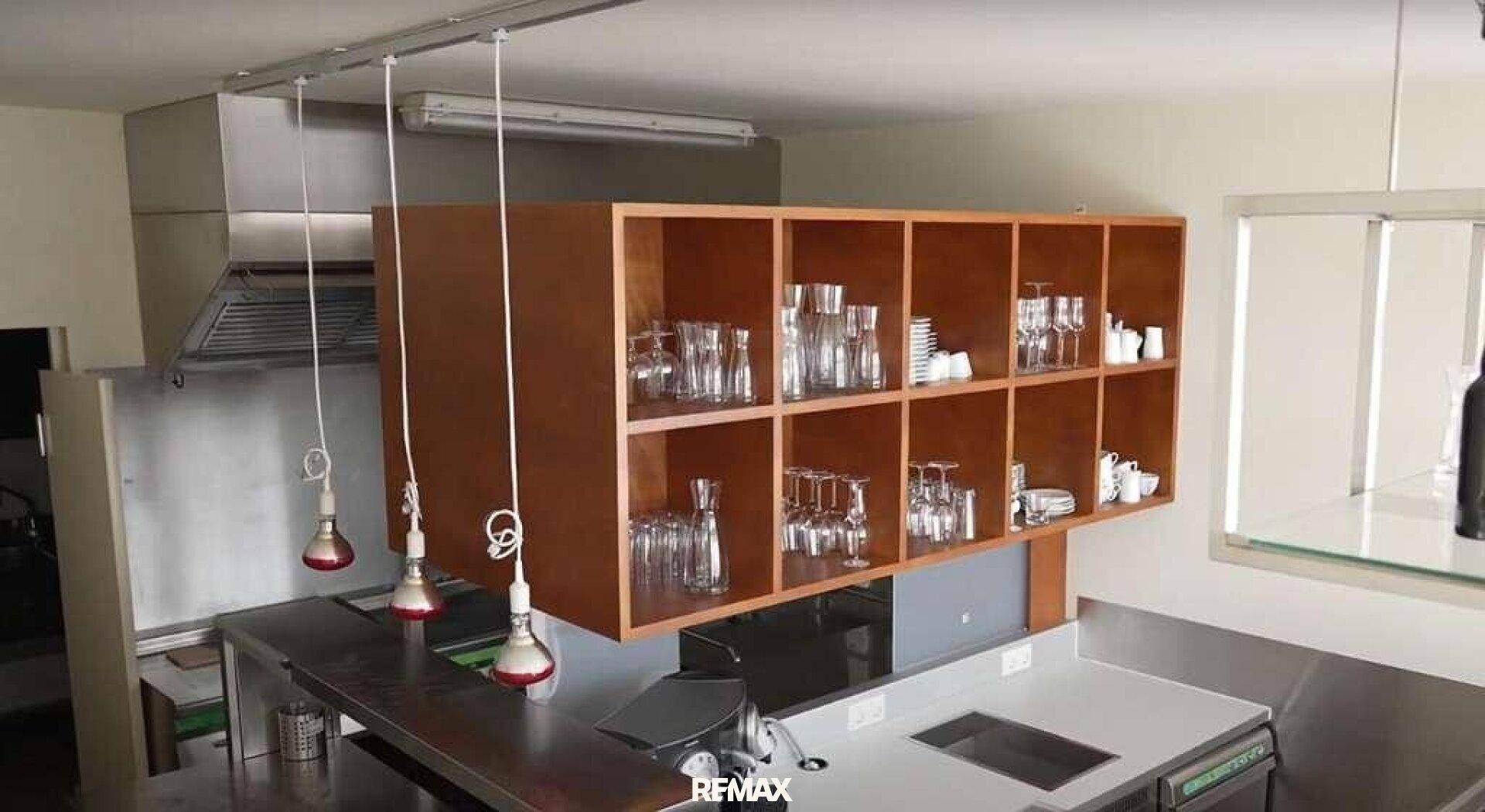 Professionelle Küche mit Edelstahlgeräten, Dunstabzugshaube und Holzregalen für Gläser.