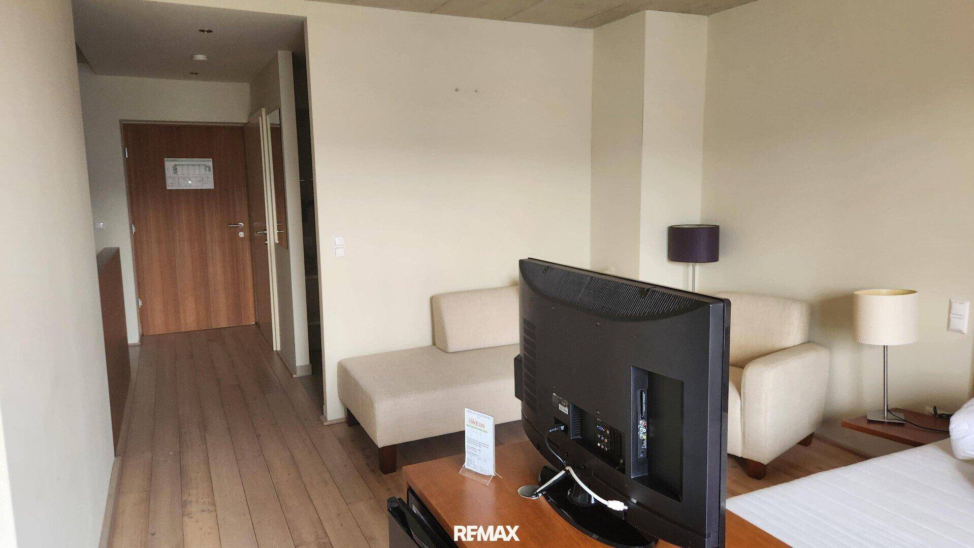Helles Schlafzimmer mit Holzboden, beigem Sofa und Flachbildfernseher.