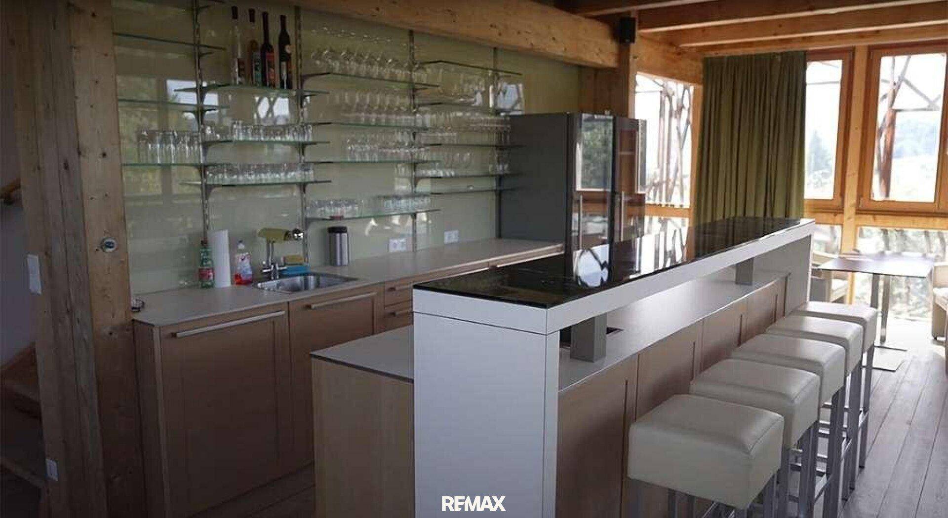 Moderne Bar mit Theke, Hockern und Glasregalen in einem Raum mit Holzbalken.