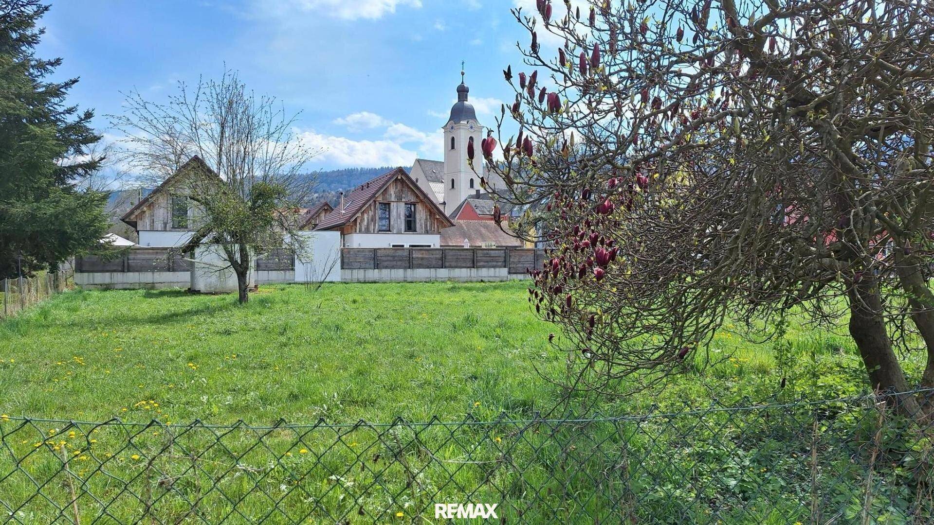 Grünfläche mit Zaun im Vordergrund und malerischem Blick auf eine Kirche und umliegende Häuser.