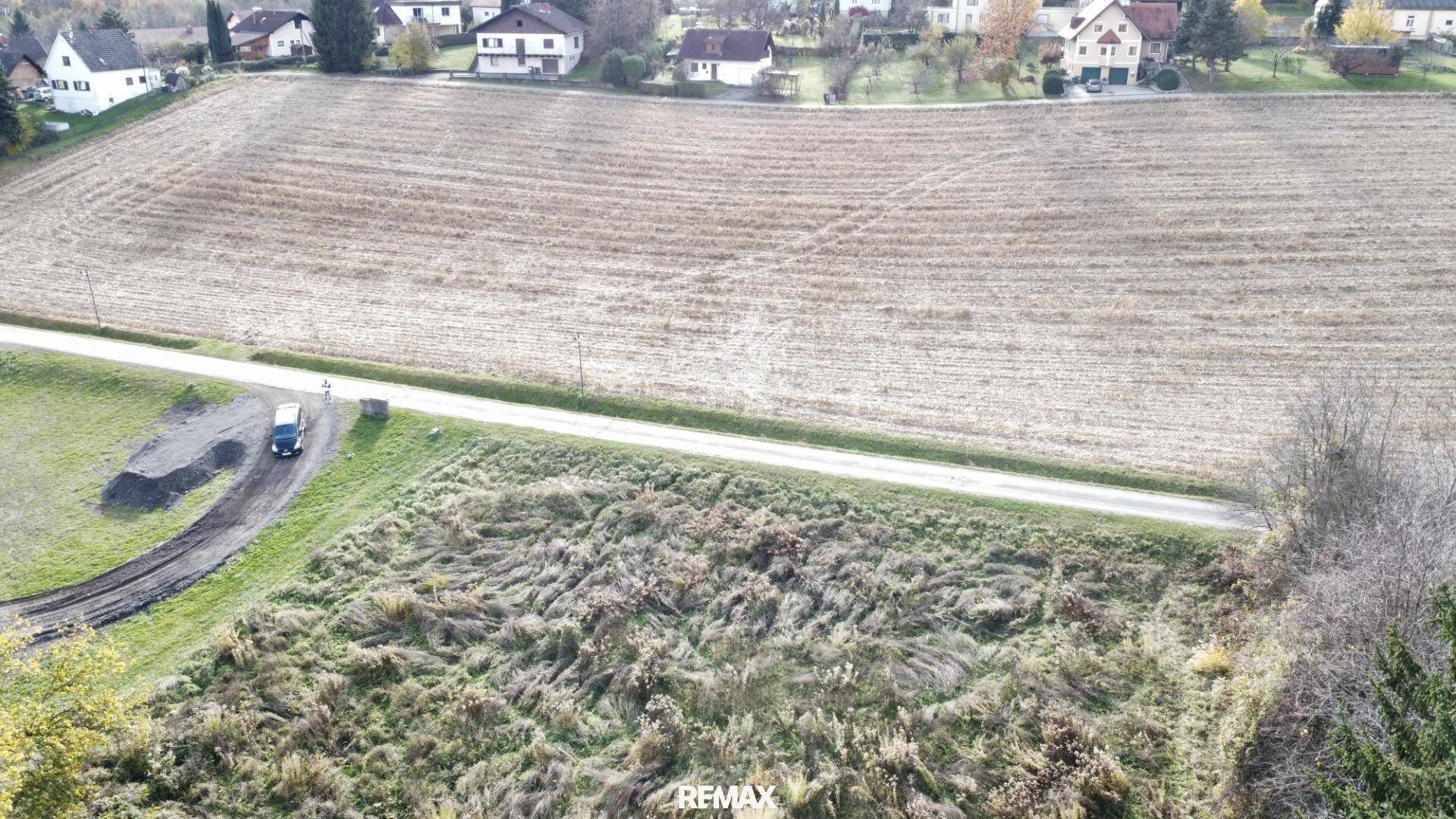 Luftaufnahme eines Grundstücks mit angrenzendem Feld und Wohnbebauung in der Ferne.