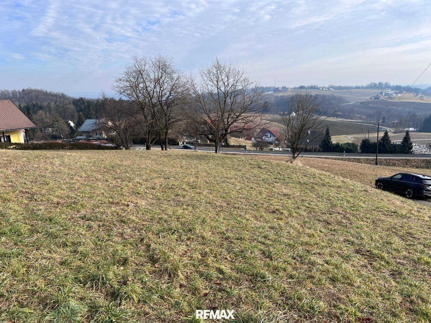 Grünes Grundstück mit leichter Neigung und Panoramablick auf die ländliche Umgebung und vereinzelte Häuser.