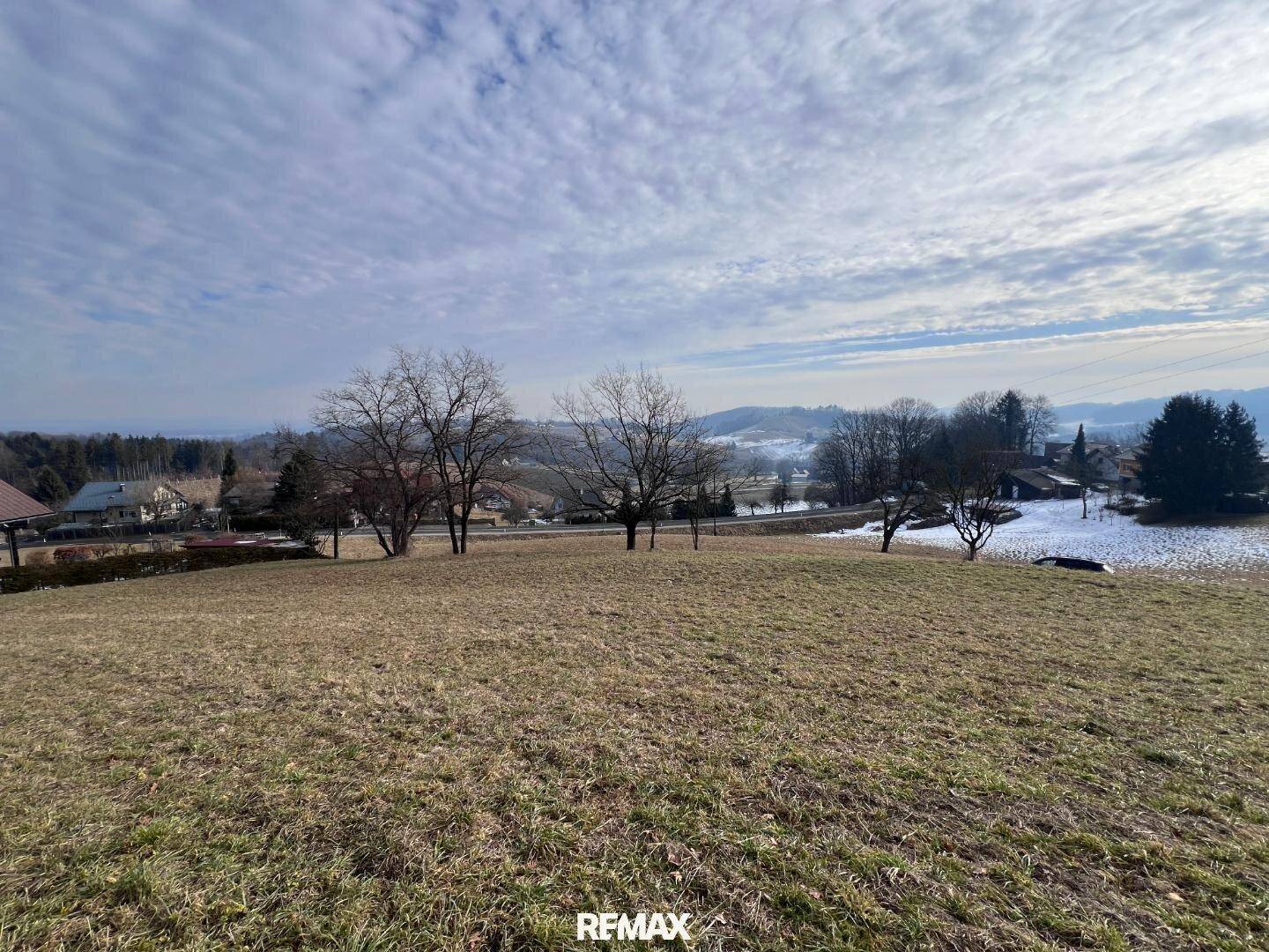 Offenes Wiesengrundstück mit Blick auf die winterliche Landschaft und vereinzelte Schneefelder.