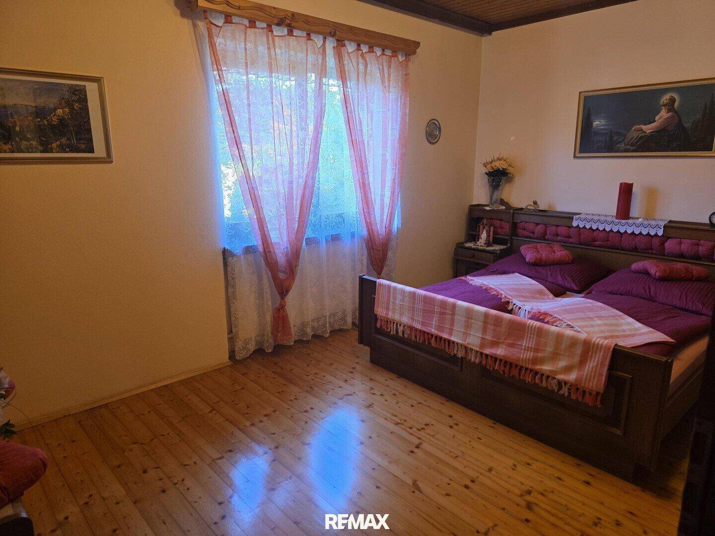 Schlafzimmer mit Holzboden, Holzdecke und einem großen Bett, hell durch das Fenster.