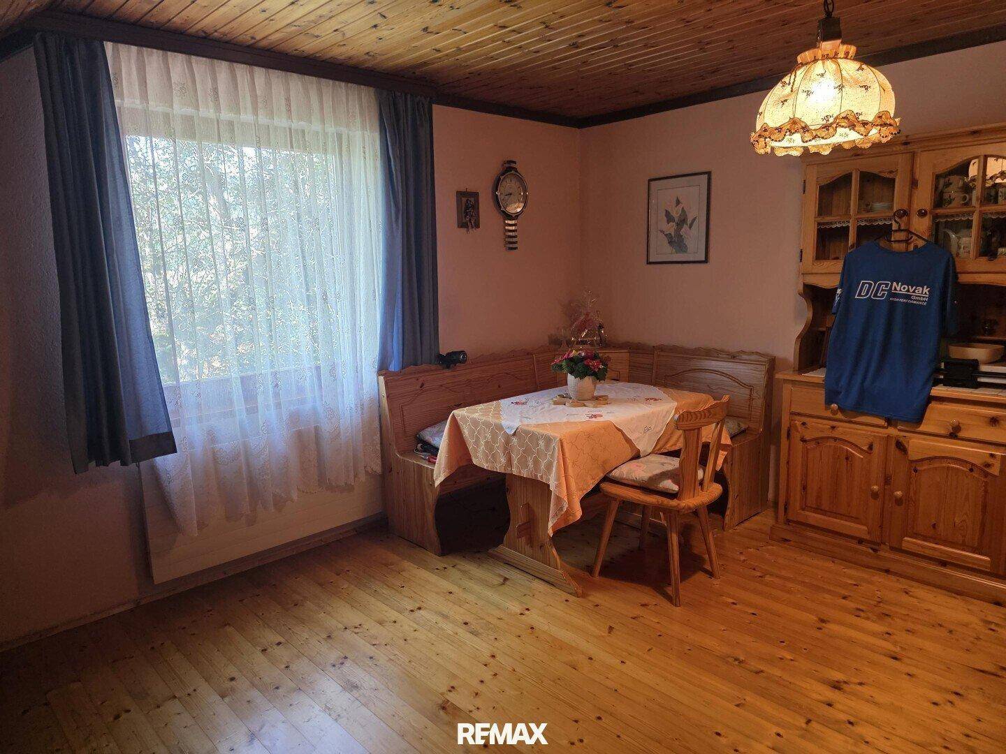 Esszimmer mit Holzboden, Holzdecke und traditionellen Holzmöbeln, hell durch das Fenster.