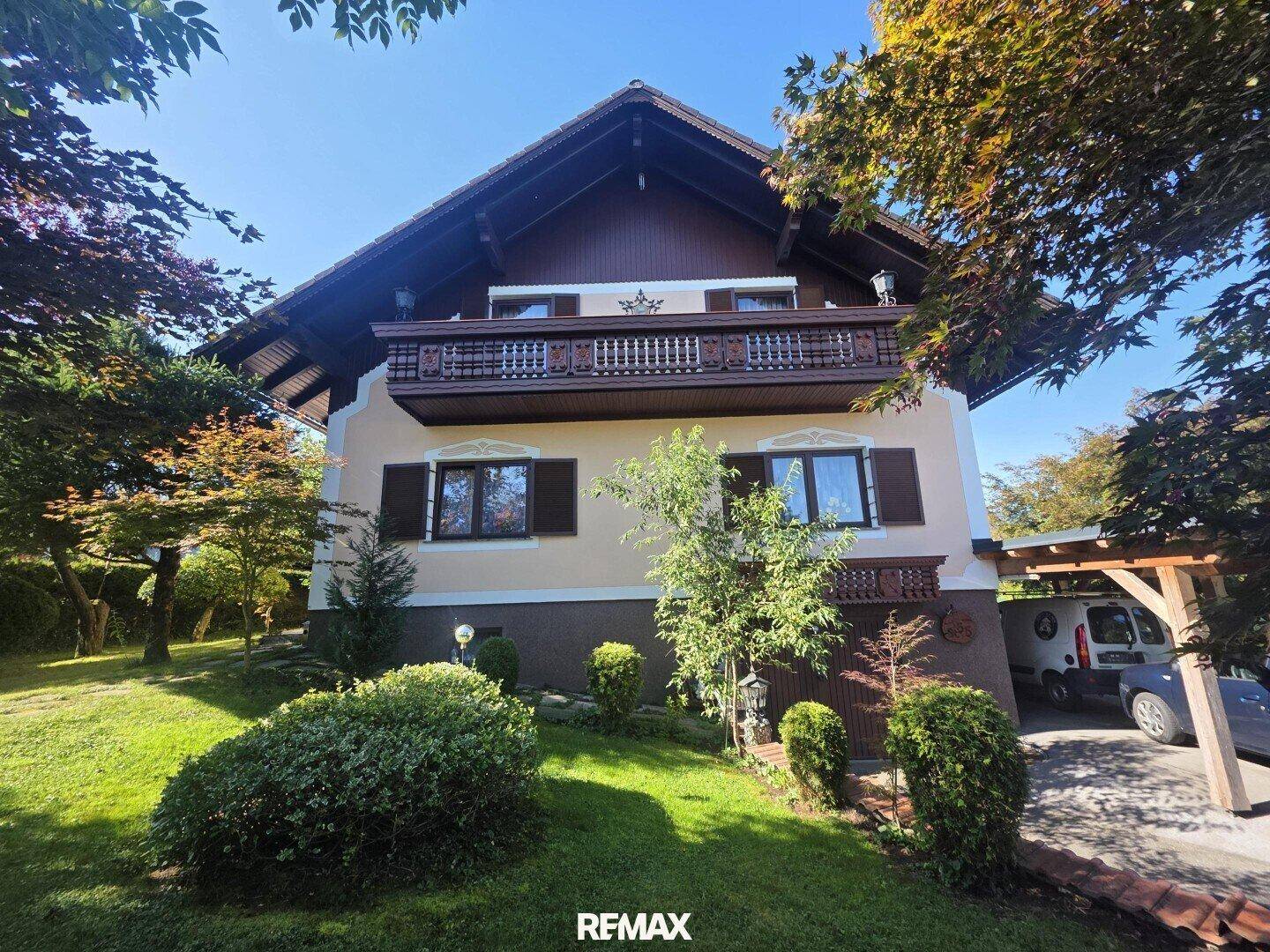 Traditionelles Wohnhaus mit Holzbalkon und gepflegtem Vorgarten unter blauem Himmel.