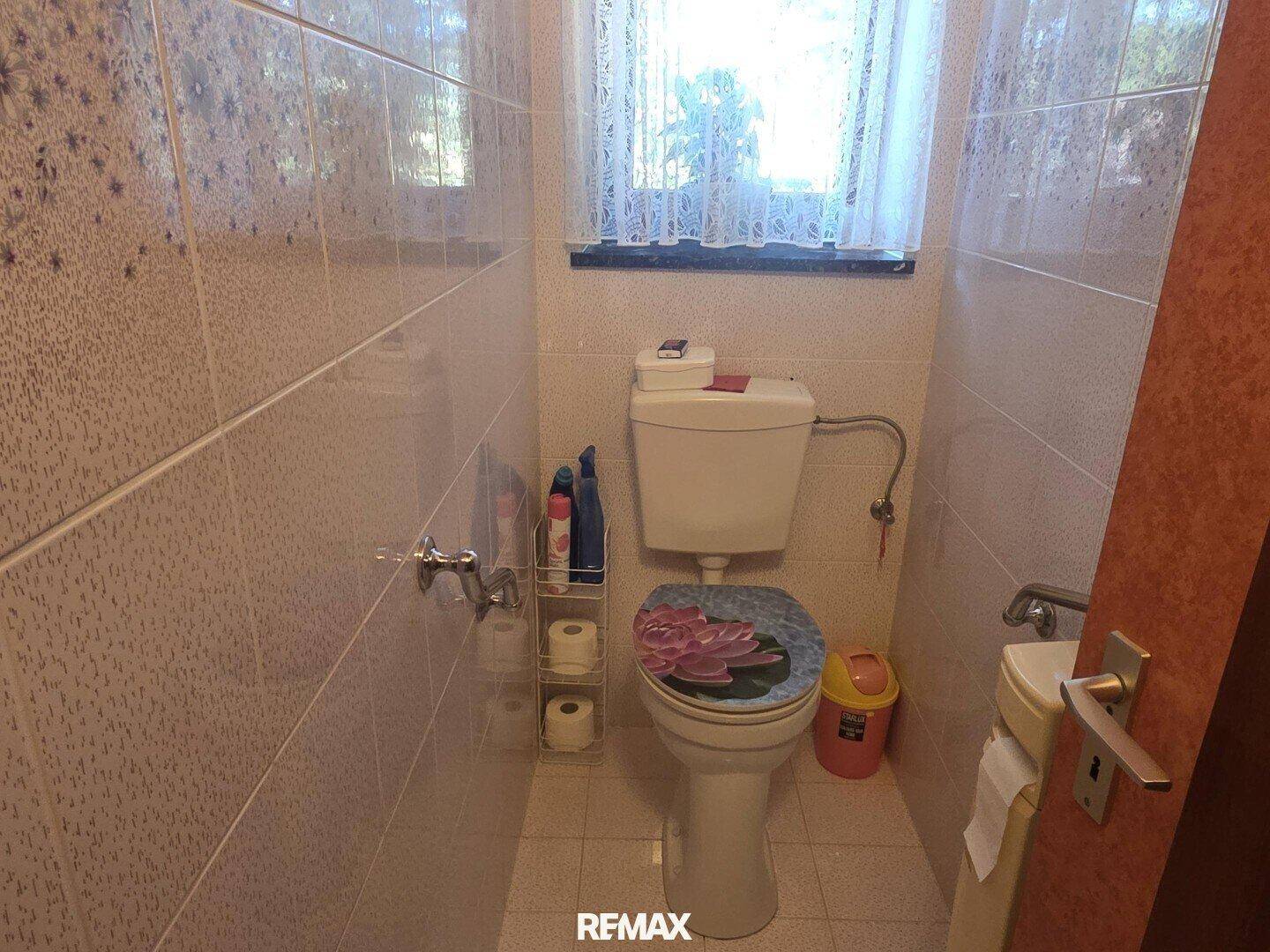 Kleines WC mit Fliesen an Wänden und Boden, ausgestattet mit Toilette und kleinem Waschbecken.