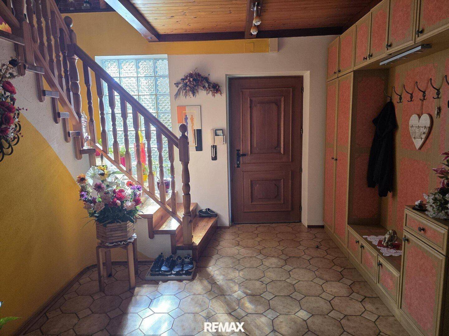 Heller Eingangsbereich mit Holztreppe, Garderobe und gemustertem Fliesenboden.