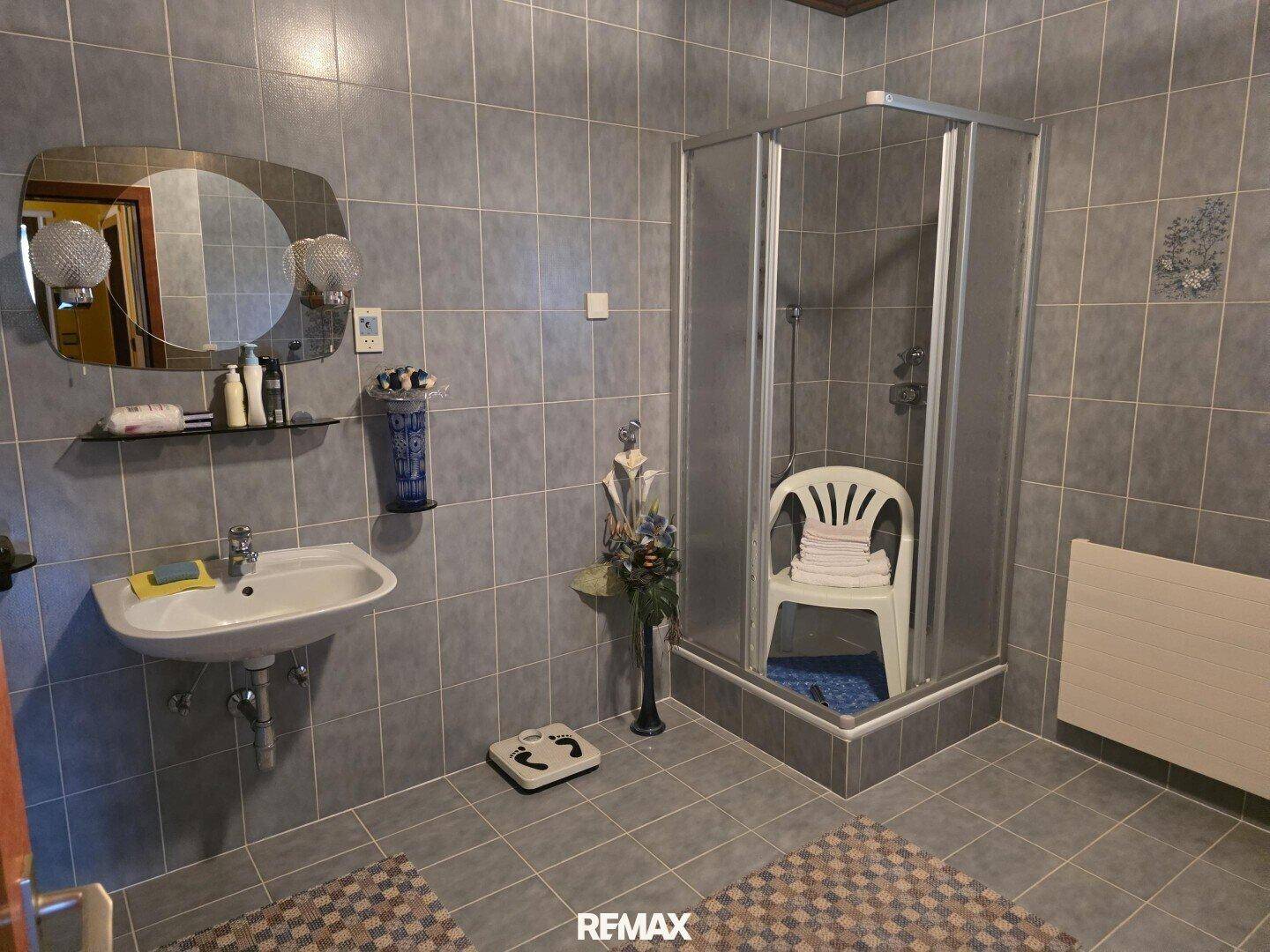 Badezimmer mit grauen Fliesen, Duschkabine und Waschbecken, hell durch das Fenster.