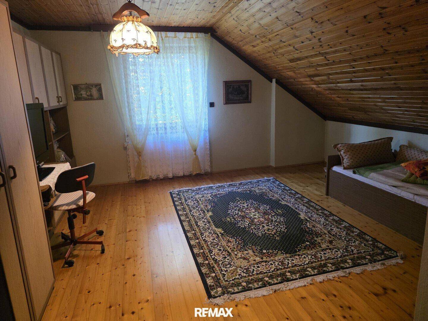 Schlafzimmer im Dachgeschoss mit Holzboden, schräger Holzdecke und großem Teppich.