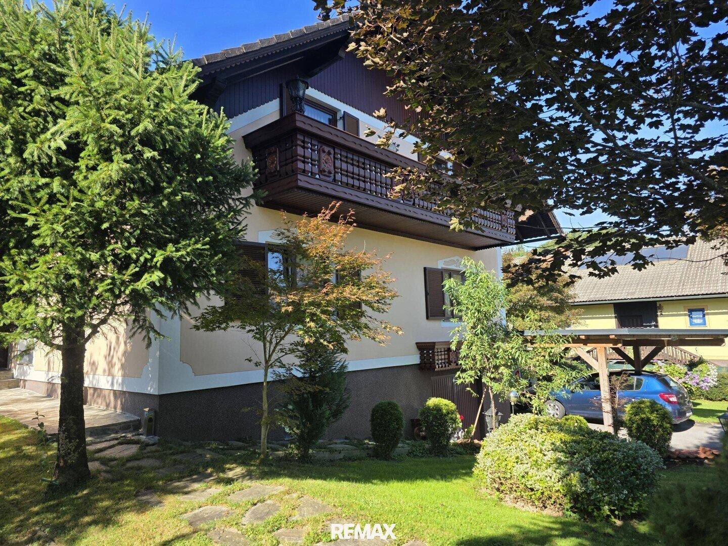 Charmantes Haus mit traditionellem Holzbalkon, umgeben von einem gepflegten Garten.