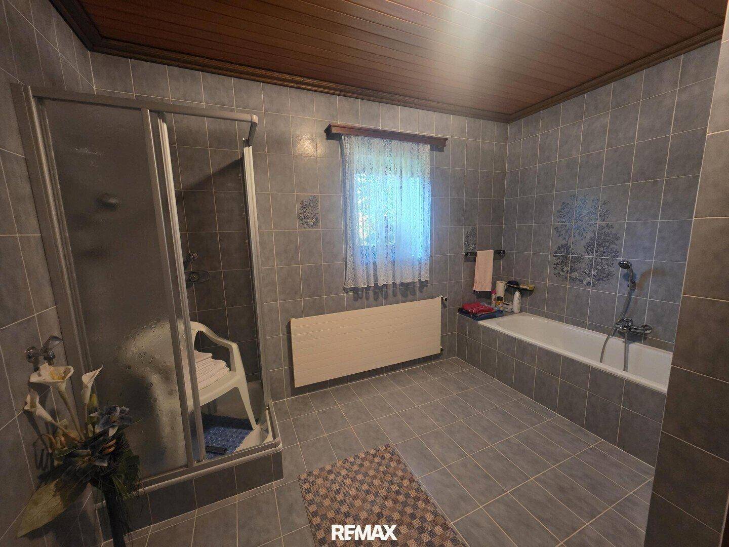 Geräumiges Badezimmer mit grauen Fliesen, Duschkabine und Badewanne.