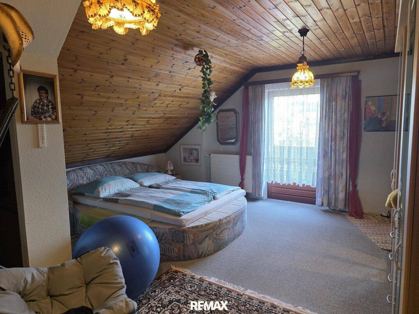 Gemütliches Dachgeschoss-Schlafzimmer mit rundem Bett, Holzboden und Balkonzugang.
