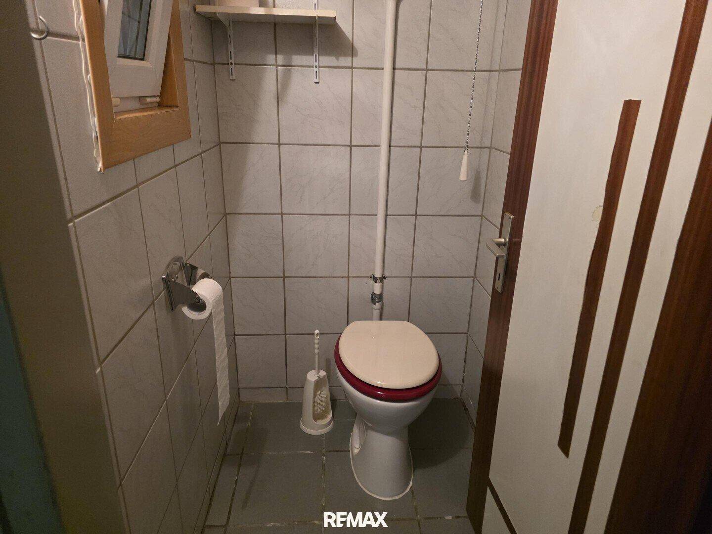 Kleines Gäste-WC mit Fliesenboden, Fenster und einfacher Ausstattung in hellem Grau.