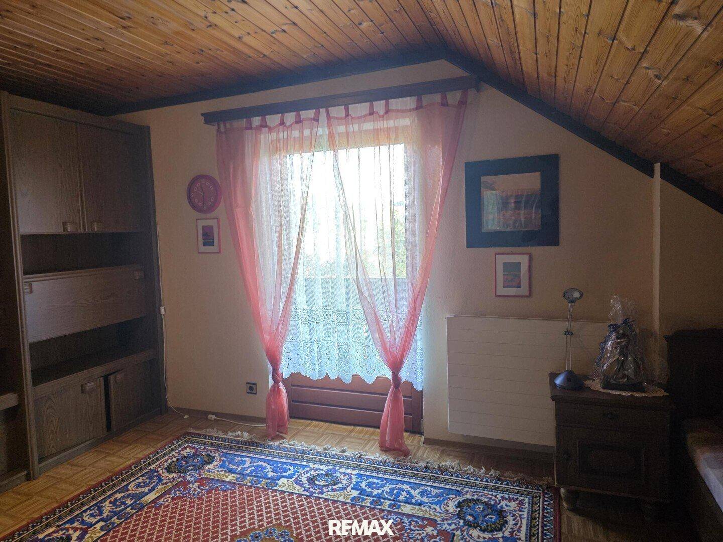 Dachgeschoss-Schlafzimmer mit Holzboden, schräger Decke und Zugang zu einem Balkon.