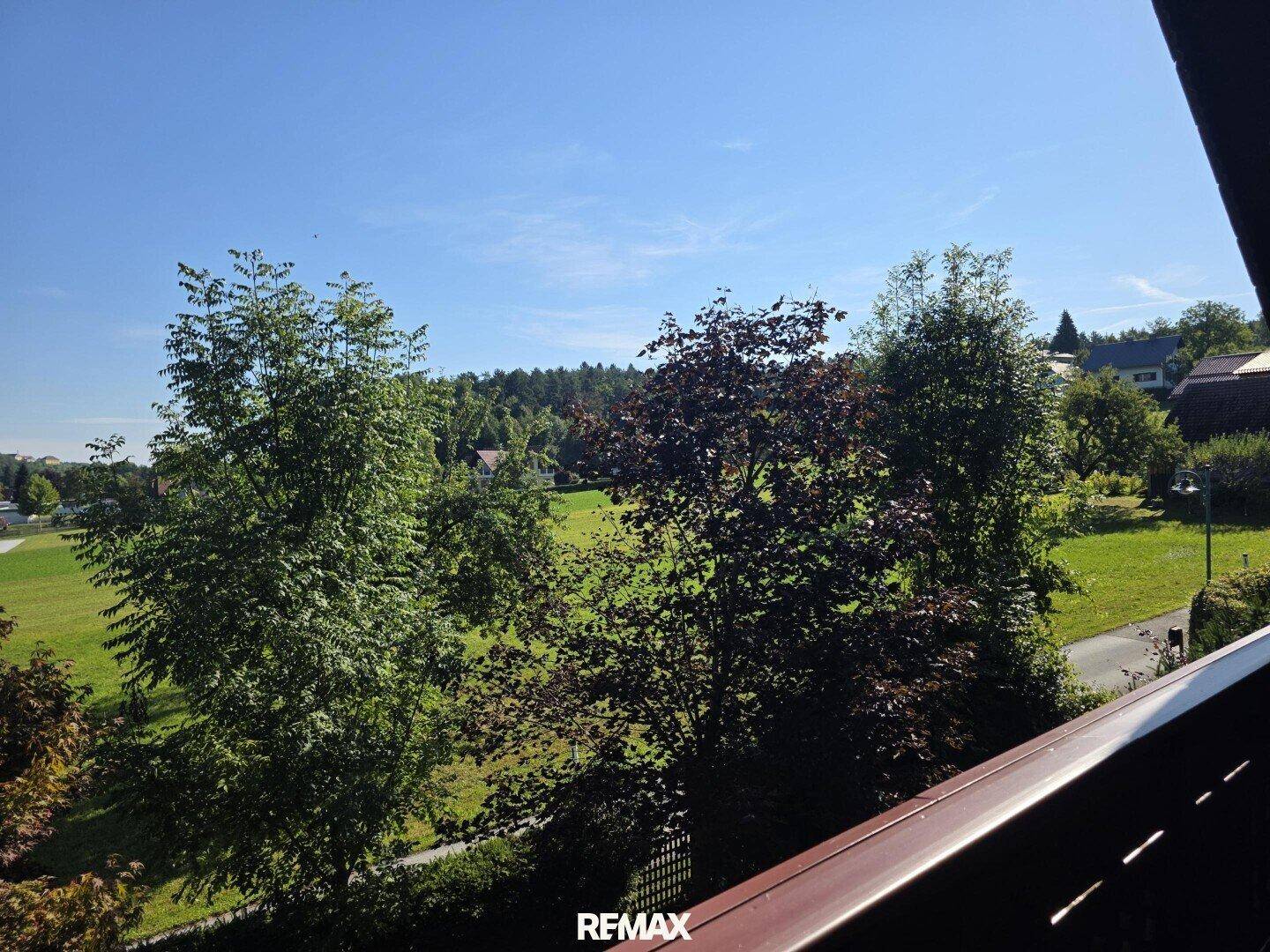 Panoramablick vom Balkon über weite Felder und bewaldete Hügel unter blauem Himmel.