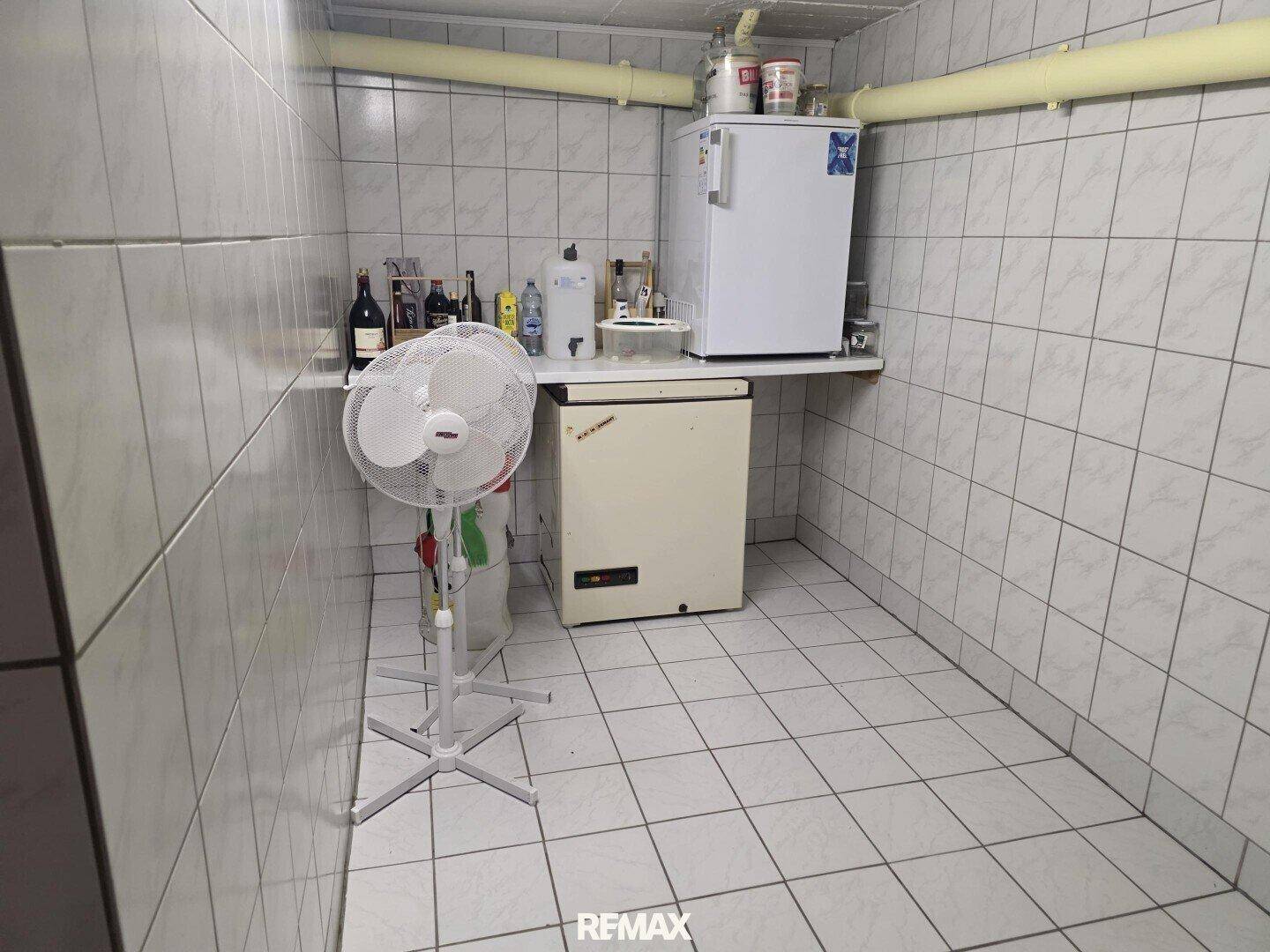 Kellerraum mit Fliesenwänden und -boden, ausgestattet mit Kühlschrank und Gefriertruhe.