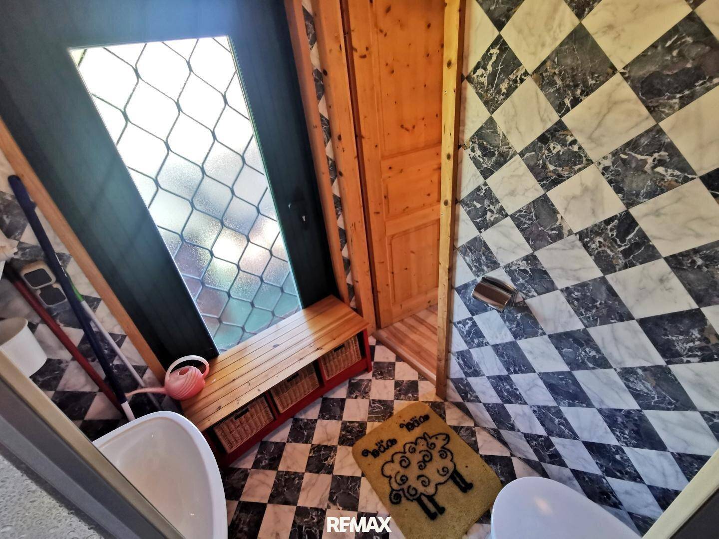 Badezimmer mit markanten Schwarz-Weiß-Fliesen, WC und einem Fenster mit Gittermuster.