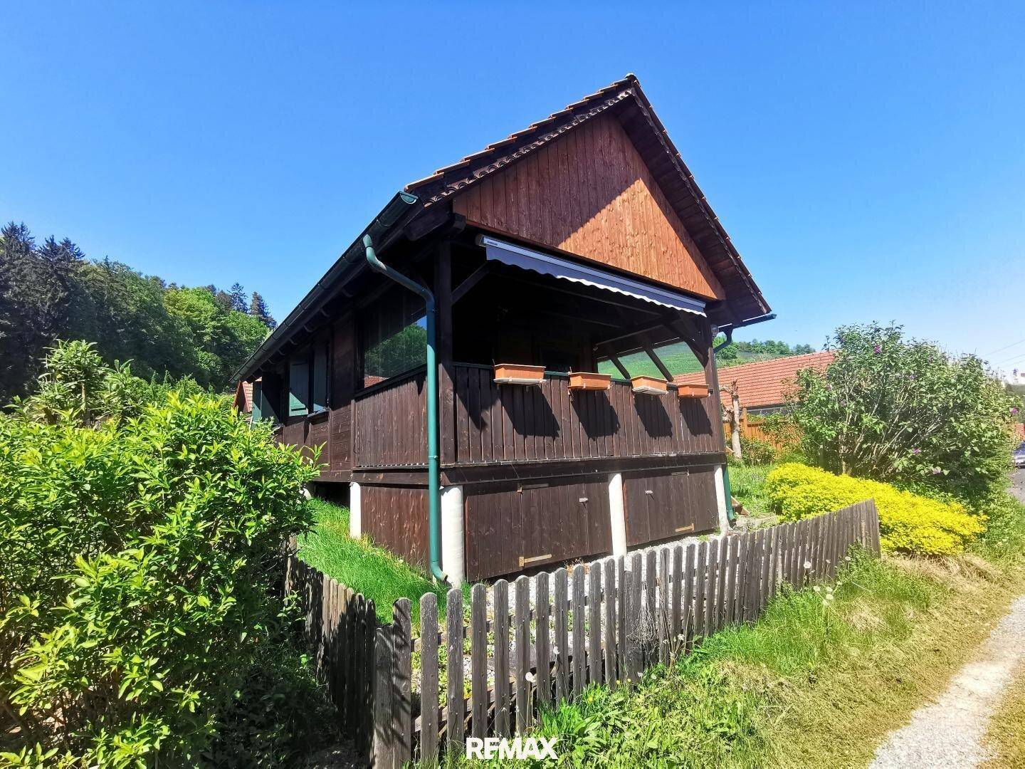 Charmantes Holzhaus mit überdachtem Balkon und umgebender grüner Vegetation.