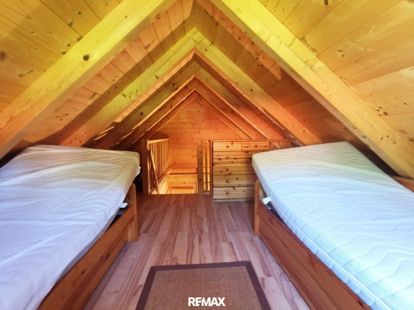 Dachgeschoss-Schlafzimmer mit Holzbalken, zwei Betten und Blick auf die offene Treppe.