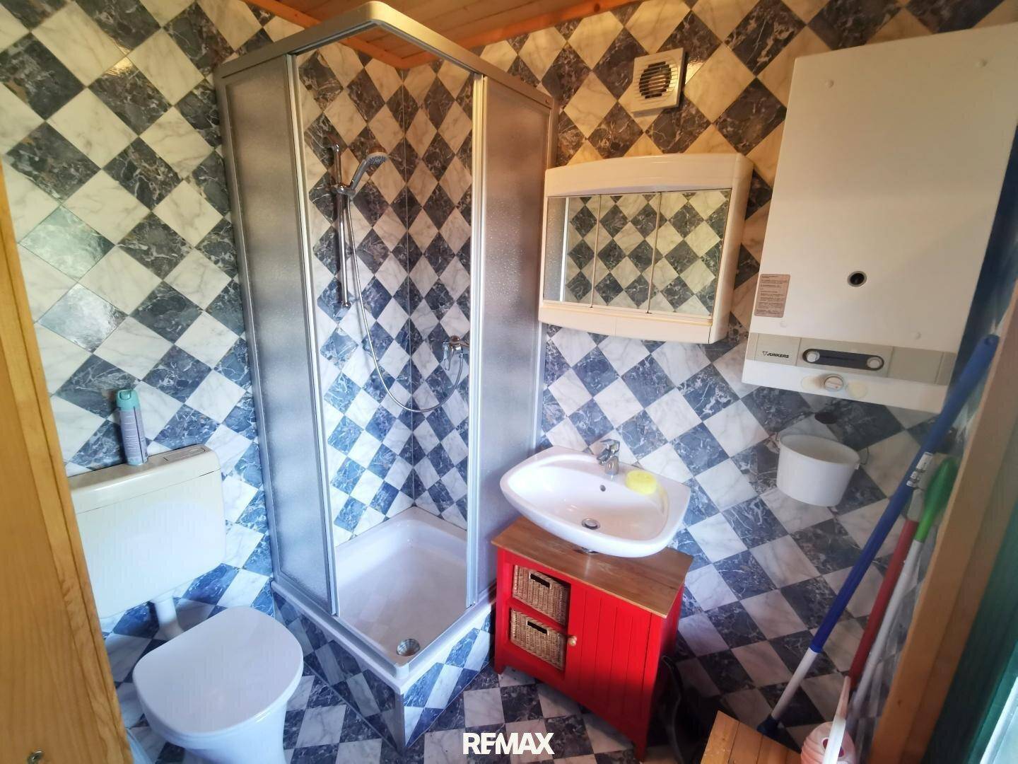 Kleines Badezimmer mit Duschkabine, Waschbecken und WC, gefliest in Schwarz-Weiß-Muster.