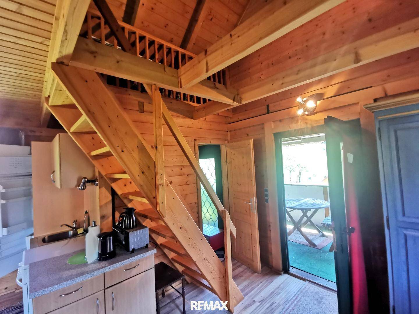 Rustikaler Wohnbereich mit Holzvertäfelung, offener Treppe zum Dachboden und Zugang zum Balkon.