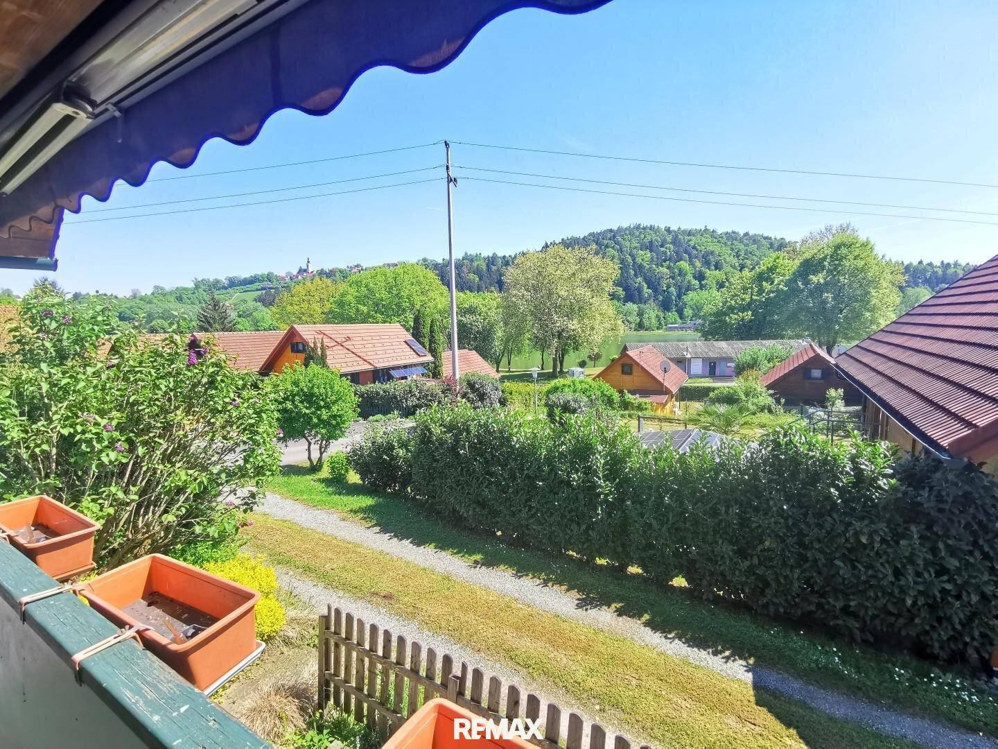 Weitblick über die grüne Landschaft mit Häusern und einem See im Hintergrund von einem Balkon aus.