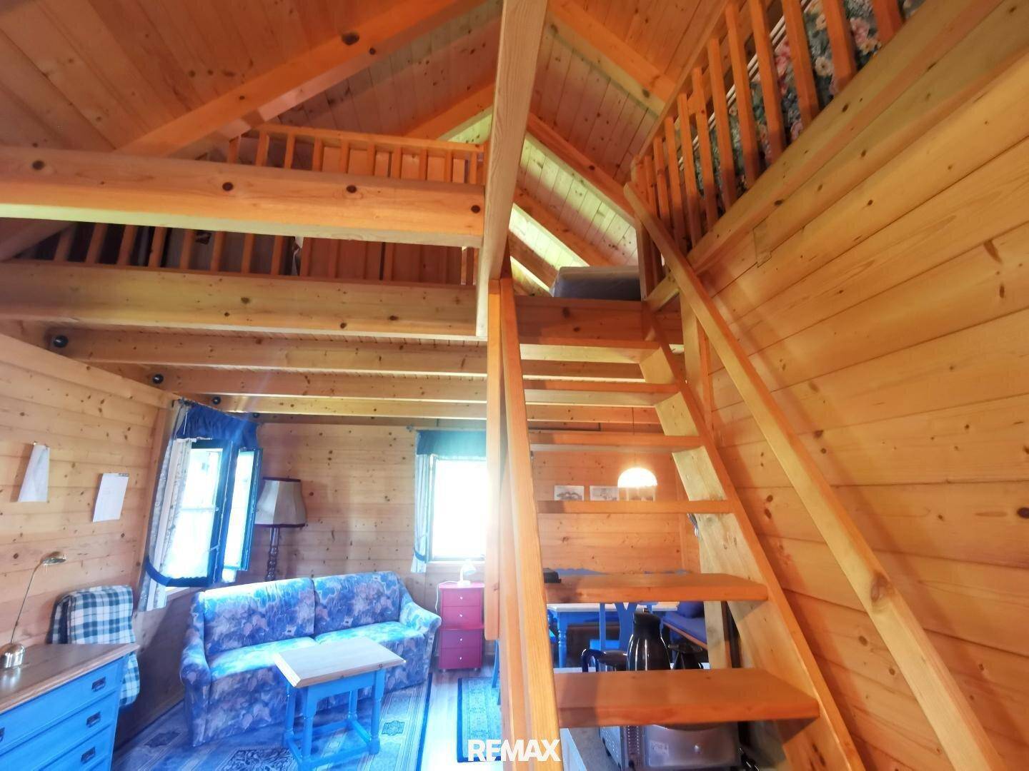 Offener Wohnbereich mit Holzvertäfelung und einer Holztreppe, die zum oberen Schlafbereich führt.