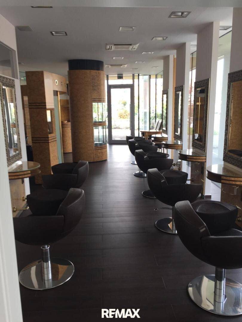 Geräumiger Friseursalon mit vielen Stylingplätzen, dunklem Boden und Blick auf den Eingangsbereich und die Fensterfront.