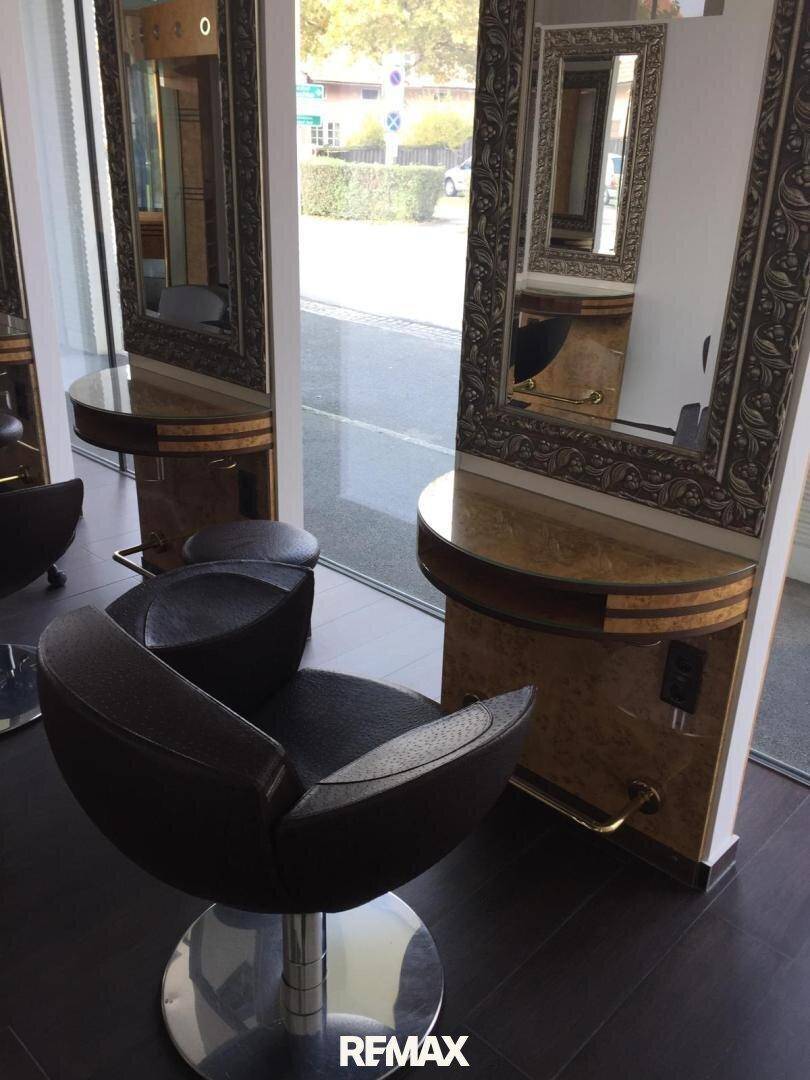 Detailansicht eines Stylingplatzes im Friseursalon mit modernem Stuhl, großem Spiegel und Holztisch für Utensilien.