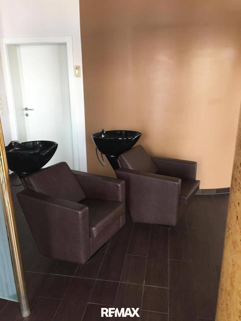 Bereich zum Haarewaschen in einem Friseursalon mit zwei bequemen Sesseln und passenden Waschbecken an der Wand.