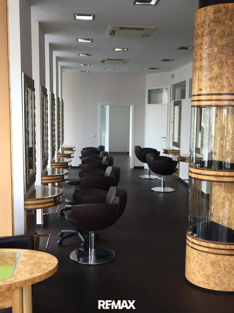 Innenansicht eines Friseursalons mit mehreren Stylingstühlen, großen Spiegeln und dunklem Bodenbelag, bereit für Kunden.