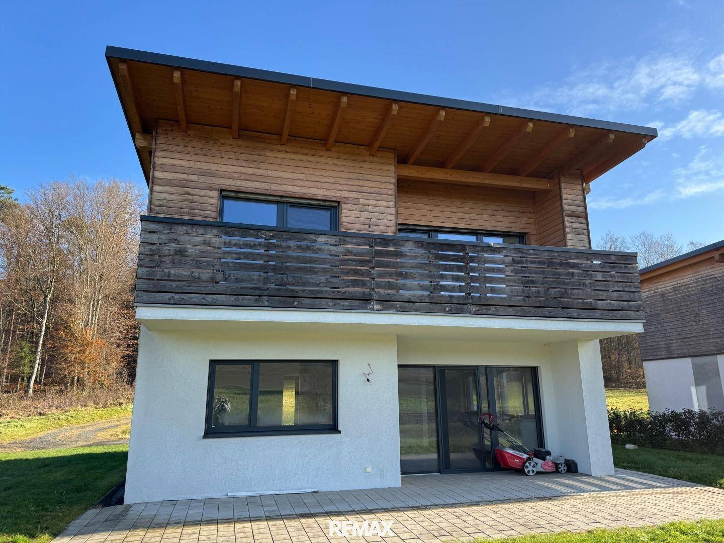 Moderne Hausfassade mit Holzverkleidung im Obergeschoss und weißem Putz im Erdgeschoss.