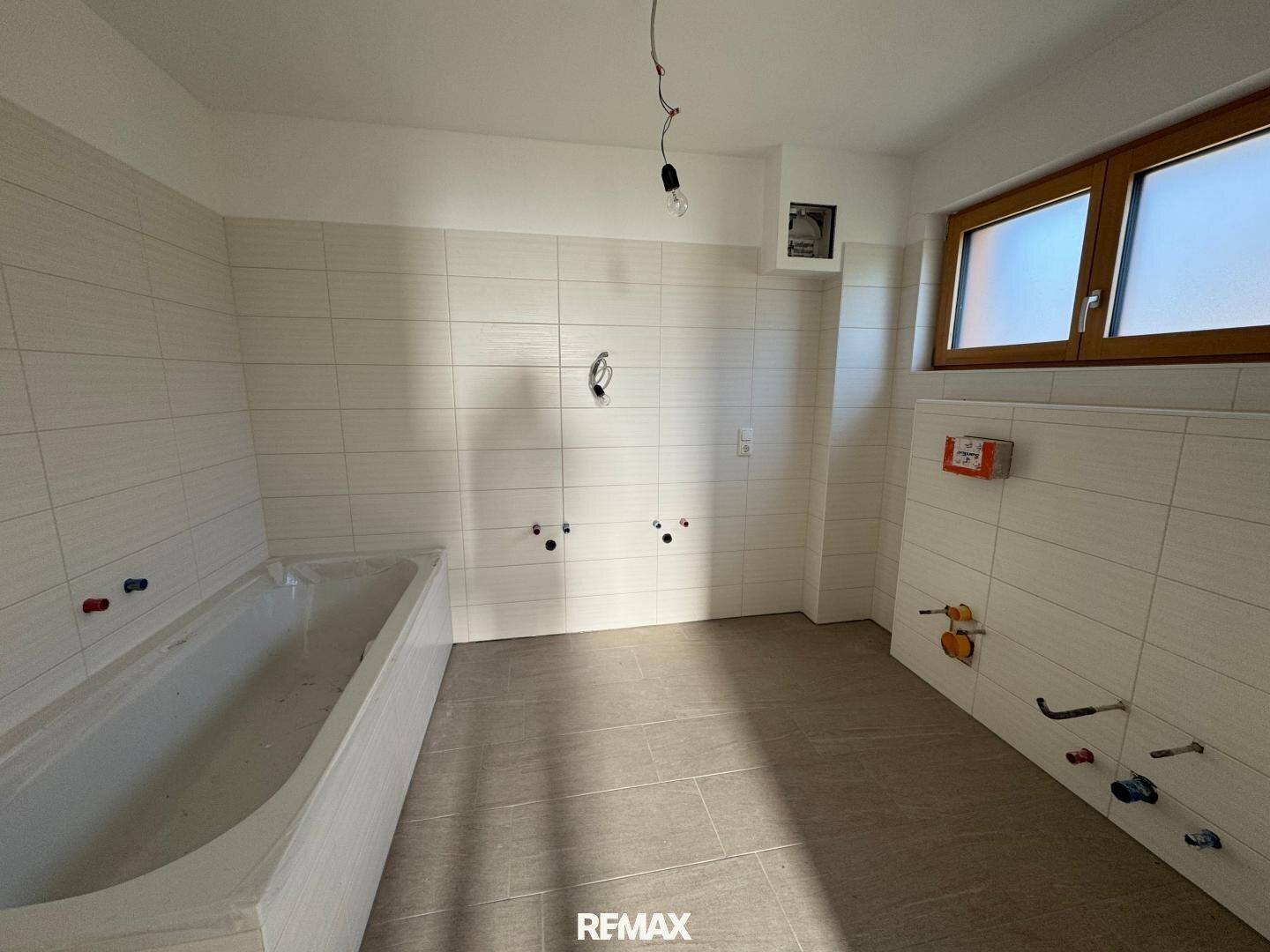 Unfertiges Badezimmer mit Badewanne, Fliesen an den Wänden und einem Fenster.